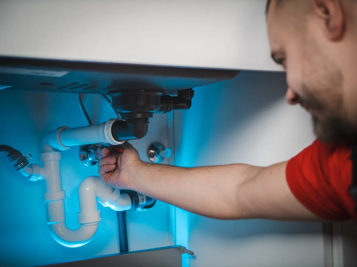 Mani al lavoro su un sifone, con la luce blu della lampada da lavoro